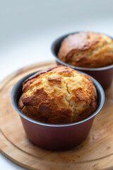 Two muffins in a pan on a wooden cutting board. The muffins are golden brown and look freshly...