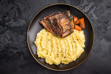 Braised beef short ribs resting on a bed of creamy mashed potatoes, creating an inviting culinary scene. black background. top view