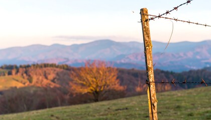 Rustic wooden fence post in a field, mountains softly blurred in the background at sunset