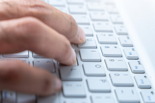 A close-up shot of a person's hands typing on a white laptop keyboard. Working, writing, programming, or communicating in a digital environment concept.