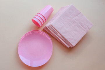 Set of pink disposable plastic cups and plates arranged neatly on a light beige background. Festive tableware with subtle shimmer for parties or celebrations