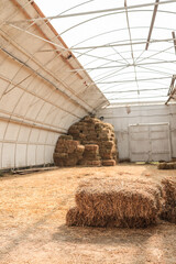Interior view of a large barn with stacks of hay bales arranged on the floor and against the walls,...