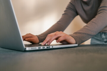 Fototapeta premium Close-up of person typing on laptop keyboard, wearing long-sleeved shirt, working at desk in indoor setting