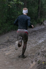 Athlete running puddles of mud in heavy rain during forest marathon