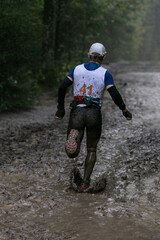 Athlete running muddy forest trail during marathon in heavy rain