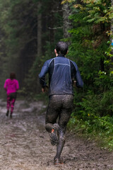 Rear view athlete running muddy forest trail during marathon in heavy rain