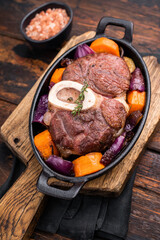Hearty ossobuco slow cooked to perfection, showcasing succulent osso buco shank meat and aromatic herbs in a comforting stew. wooden background. top view