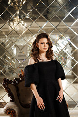 a woman in an elegant black dress with puffy sleeves. She stands indoors against a mirrored wall...