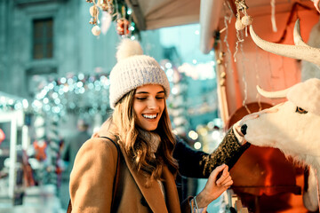 Happy woman having fun with a reindeer decoration at a Christmas market. Young person smiling and...