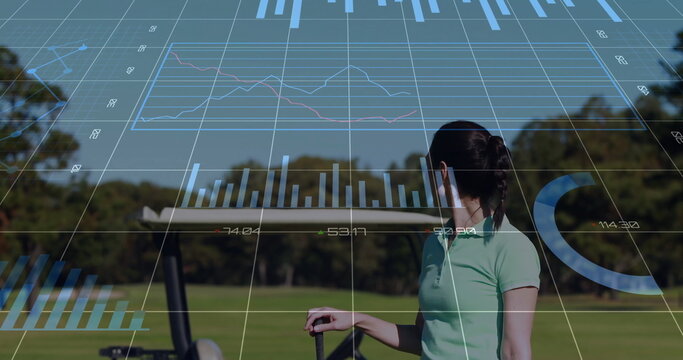 Standing female golfer analyzing real-time analytics on golf fairway, with golf club and push cart