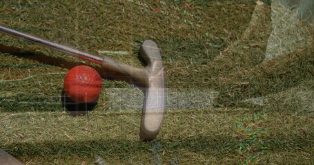 Resting putter head near red golf ball on black tee on putting green, with grid overlay