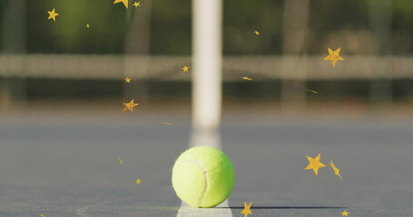 Resting tennis ball sitting balanced on painted hardcourt, with net post, rope and star graphics