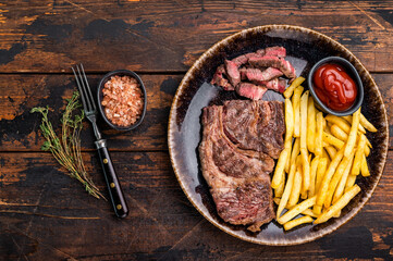 Dinner with grilled Chuck eye roll steak and french fry on a plate. wooden background. top view