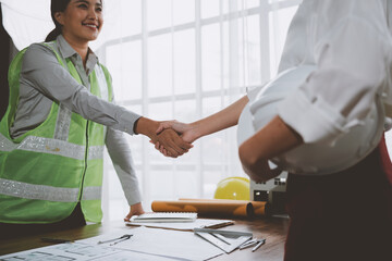 Engineers shaking hands over blueprint on desk