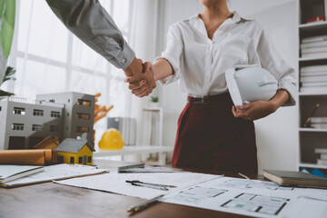 Architects shaking hands over building model and blueprint plans