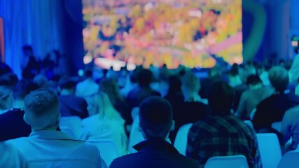 Large group of people attending an indoor conference with a colorful display screen and engaging atmosphere
