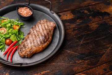 Grilled striploin steak, strip loin beef meat steak on a steel tray. wooden background. top view