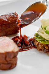 A creative gourmet dish with a piece of meat, a red sauce, and a side of vegetable tartare topped...