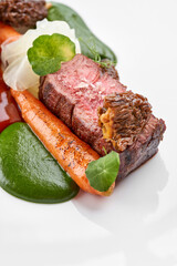 A beautifully plated steak dish with two pieces of medium-rare meat, roasted carrots, and two different sauces, served on a round white plate.