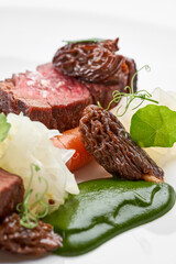 A beautifully plated steak dish with two pieces of medium-rare meat, roasted carrots, and two different sauces, served on a round white plate.