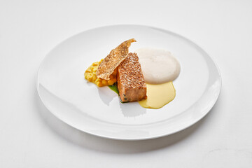 A fine dining dish with a piece of white fish steak, a crispy skin garnish, two different sauces, and a yellow vegetable purée on a white plate.