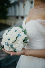 bride in a white modern dress holds a bouquet of white roses in her hands on her wedding day