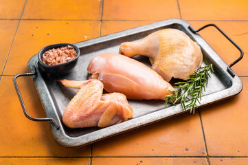 A tray of fresh, raw chicken from an eco farm.:A metal tray with a black handle holds three pieces...