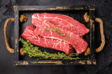 Raw skirt or machete  Steak, beef meat in wooden tray with herbs. black background. top view