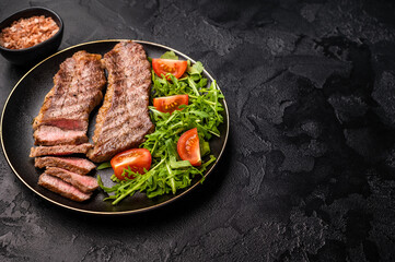 Grilled Steak from Black Angus beef meat on a plate with salad. black background. top view