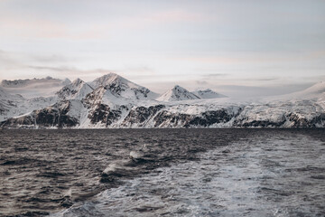 A dynamic view from a boat showing its wake on the wavy water of a fjord, with a dramatic backdrop...