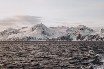 The powerful wake of a boat cuts through a dark sea, leading the eye towards a distant, panoramic...