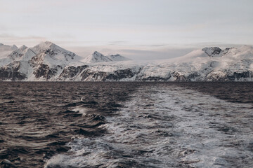 The powerful wake of a boat cuts through a dark sea, leading the eye towards a distant, panoramic...