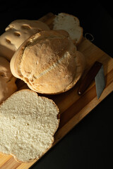 Round candeal bread loafs and slices on wooden cutting board with knife