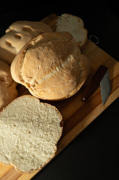 Round candeal bread loafs and slices on wooden cutting board with knife