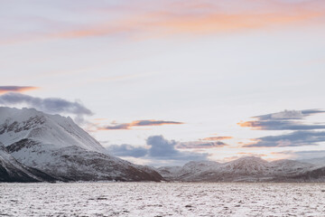 A stunning horizontal view of a Norwegian fjord at sunset, with soft, pastel-colored clouds over...