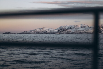 A horizontal shot from a boat, with a blurred railing in the foreground framing a view of a serene...