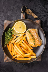 Homemade Fish and chips with roast cod whitefish fillet and fried potatoes on plate. black background. top view