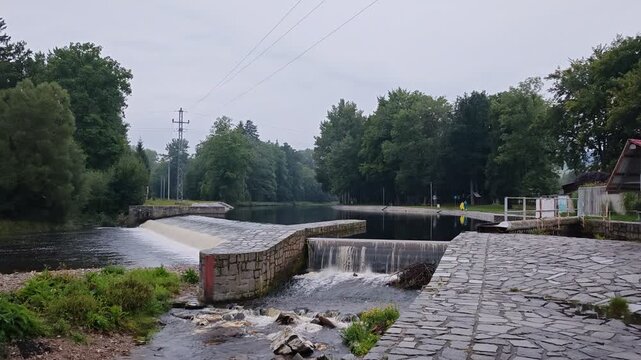 Large weir on Otava River in Sumava with flowing water and scenic surrounding nature