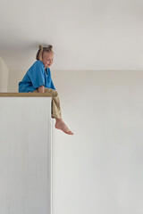 Cute kid girl sitting on a high cabinet. Child 6 years old at home