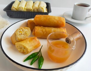 A plate of delicious Lumpia Semarang, a popular traditional spring roll from Semarang, Indonesia. The crispy deep-fried spring rolls are served with a sweet and sour sauce and fresh green chili.