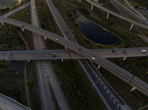 Aerial view of the intricate Sawgrass Interchange highway system casting long shadows, juxtaposed against the dark water of a nearby pond, Sunrise, Florida, United States.