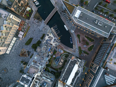 Aerial view of modern buildings casting long shadows on cobblestone streets, contrasting with the dark waters of the harbor at Aker Brygge, Oslo, Oslo, Norway.