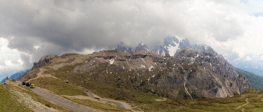 Panoramic view of Croda dei Toni from Tre Cime di Lavaredo, with rugged cliffs, cloudy sky, alpine road, and patches of snow in the Dolomites. - Powered by Adobe