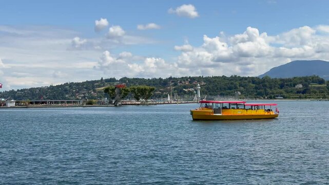 Geneva, Switzerland - 8-20-25, a Mouettes (yellow shuttle boats)part of Geneva's public transport boats is crossing the Geneva Lake, in front of P&acirc;quis Baths with hilly landscape - 4k video footage  