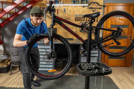 Male bicycle technician wearing gloves repairing disc brake system on mountain bike