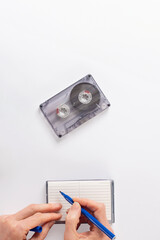 Female hands making retro songs audio playlist on blue background. Audio cassette with an empty...