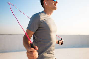 Man jumps rope on a rooftop while enjoying music and soaking in the sun's warmth during morning...
