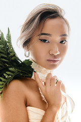 Elegant young bride in a stunning white dress poses beautifully with greenery