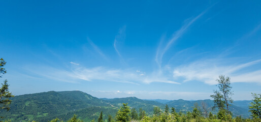 A sweeping view of lush mountains under a bright blue sky with wispy clouds, perfect for travel...
