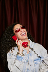 Portrait of young adult Black woman laughing with joyful expression while holding retro corded...